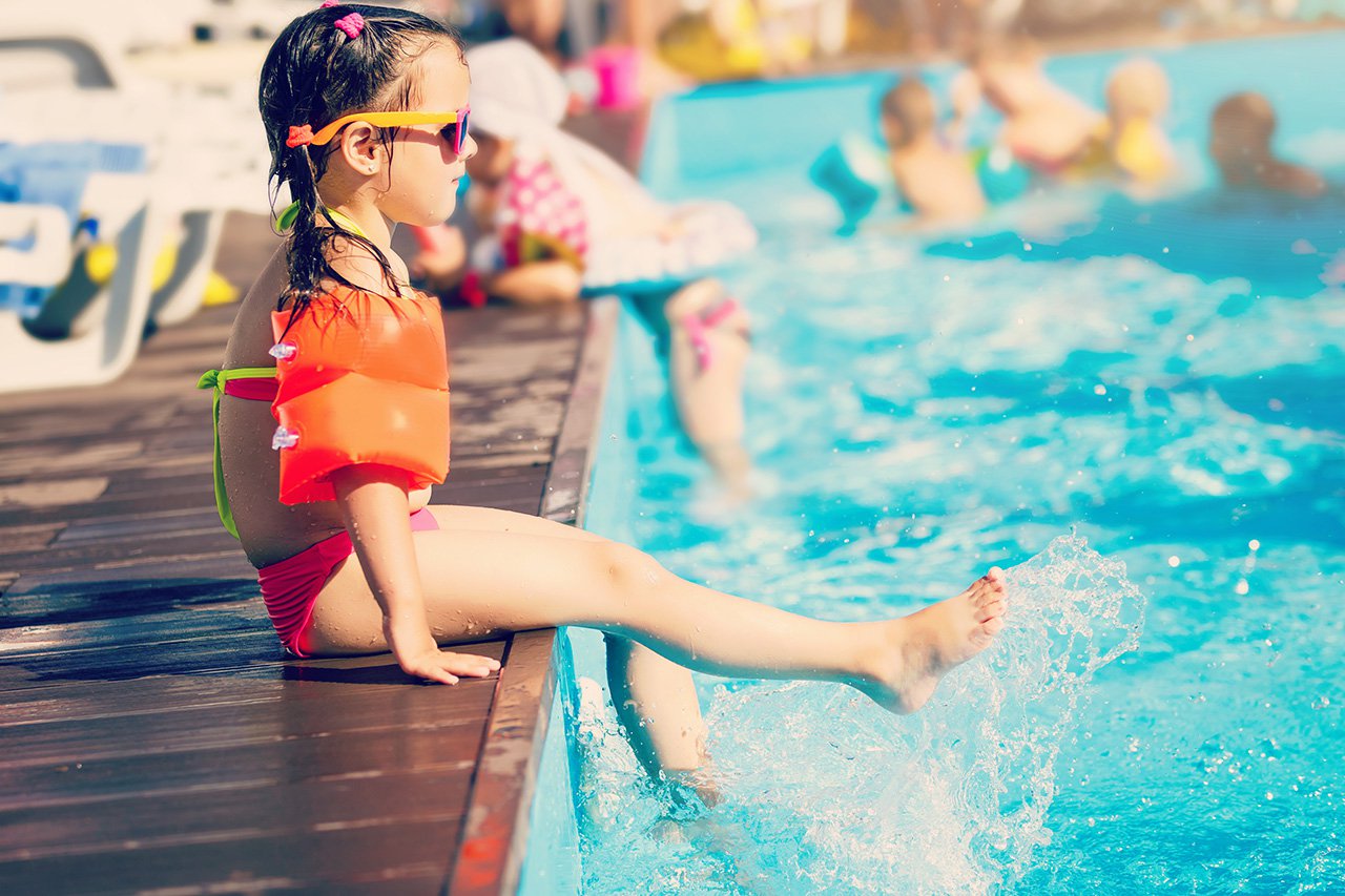 little girl playing in outdoor swimming pool jumping into water on summer